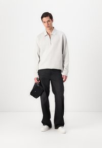 Light gray zip-up sweatshirt, black wide-leg jeans, white sneakers, and a small black bag. Smooth texture and minimalist design.