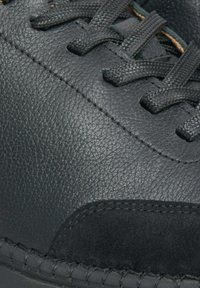 Czarna skórzana mokasyna o teksturowanym wykończeniu, z zamszowym akcentem. Okrągły nosek, kontrastowe przeszycia i płaskie sznurówki. Zbliżenie.