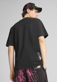 Sort kortærmet t-shirt med en glat overflade, som har en sidelabel og et kontrasterende lilla sprøjtedesign på de tilhørende shorts.
