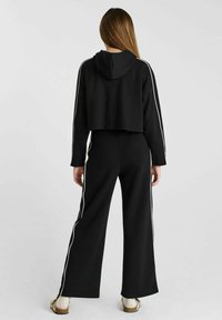 Zwarte cropped hoodie met een capuchon en witte zijstripes, gecombineerd met wijde zwarte broek met witte strepen langs de zijkanten.