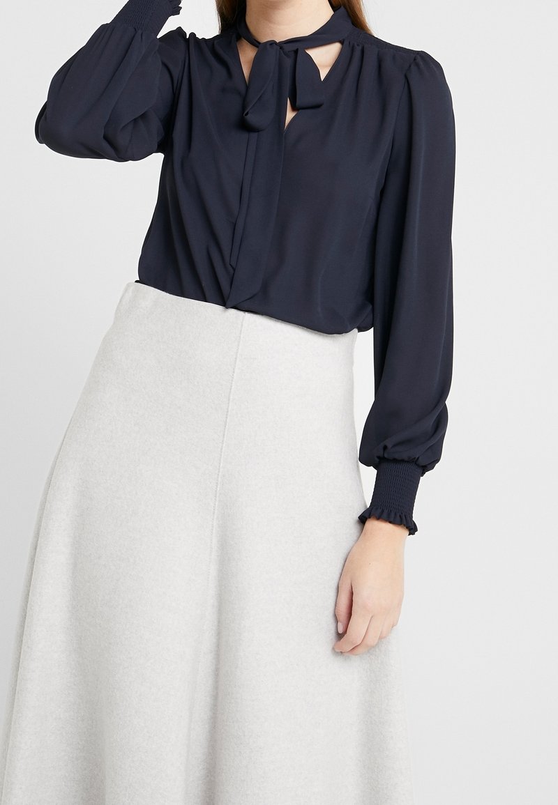 Námořnická blůza s dlouhými nabíranými rukávy a vázacími detaily na krku, spárovaná s světle šedou, volnou sukní vyrobenou z měkké látky.