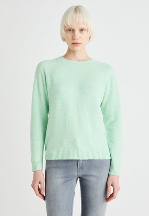 Mintgrüner Pullover mit weicher Textur, Rundhalskragen und gerippten Bündchen und Saum, kombiniert mit hellblauen Jeans.