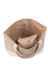 Bolso tote de lienzo en beige con rayas horizontales. El interior cuenta con un suave forro y un pequeño bolsillo con cremallera con un diseño a rayas. Detalle de cremallera dorada.