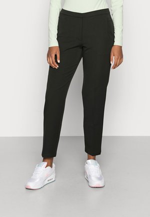 Pantalons noirs ajustés avec une coupe slim, en tissu lisse, et poches avant, assortis à des baskets blanches avec des accents roses.