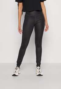 Svarta, åtsittande leggings med en slät textur och subtil sömsdetaljering, kombinerat med neutrala sneakers och en kort svart topp.