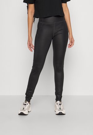 Leggings noirs ajustés avec une texture lisse et des détails de couture subtils, associés à des baskets neutres et un haut noir court.