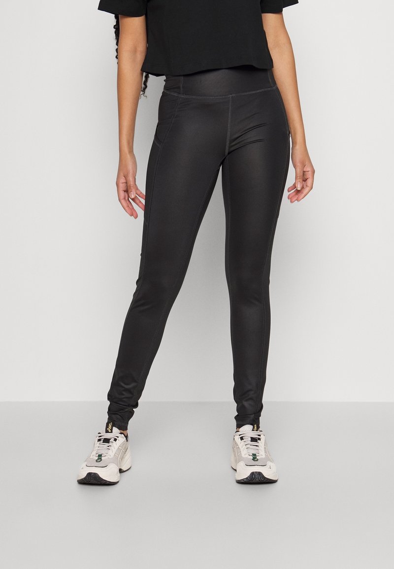 Svarta, åtsittande leggings med en slät textur och subtil sömsdetaljering, kombinerat med neutrala sneakers och en kort svart topp.