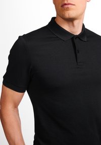 Sort polo skjorte lavet af tekstureret stof, med en foldet krave, tre-knaps placket og korte ærmer. Minimalistisk design.