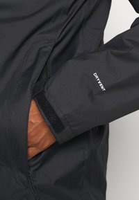 Czarna wodoodporna kurtka z regulowanym mankietem na rzep oraz kieszenią na zamek, zaprojektowana z gładką, elegancką fakturą i dopasowanym krojem.