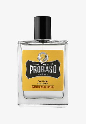 Flacon de cologne en verre transparent avec un capuchon noir et une étiquette jaune. L'étiquette présente un logo de lion et le texte "PRORASO COLONIA WOOD AND SPICE."
