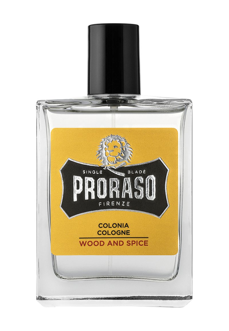 Klar glas cologne flaske med en sort kapsel og en gul etiket. Etietten har et løve-logo og teksten "PRORASO COLONIA WOOD AND SPICE."