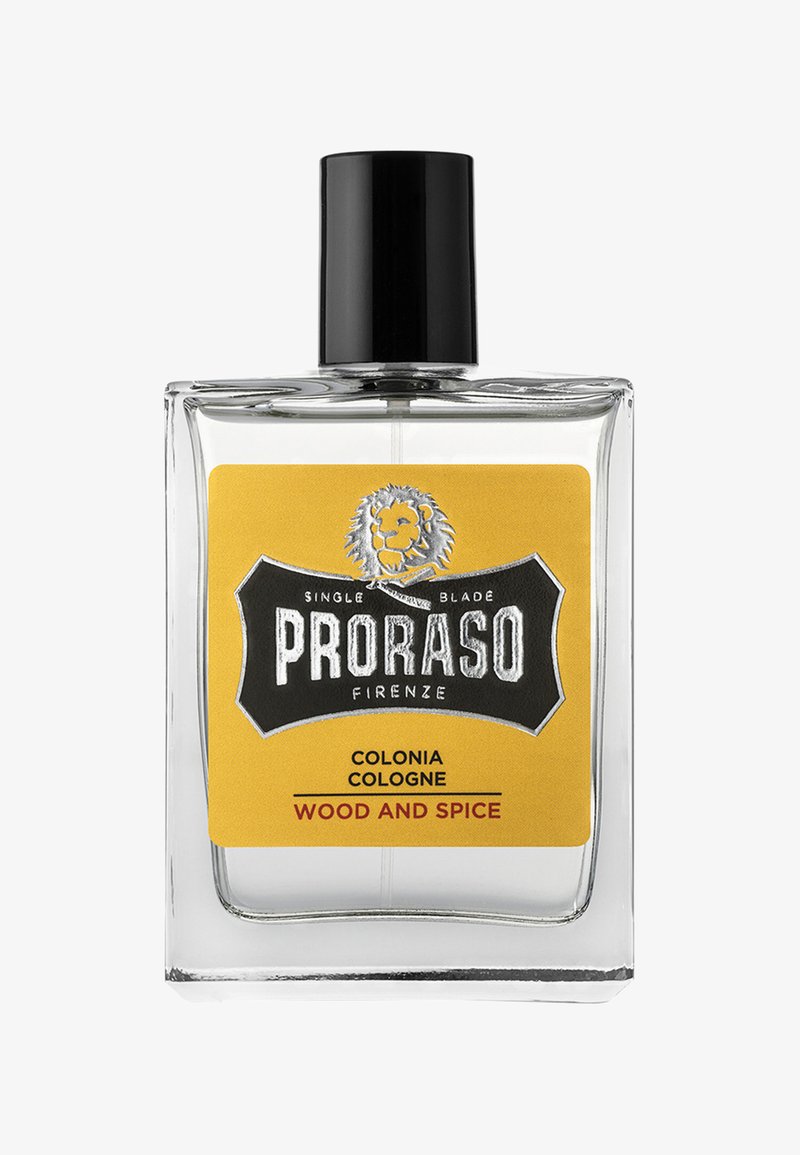 Klar glas cologne flaske med en sort kapsel og en gul etiket. Etietten har et løve-logo og teksten "PRORASO COLONIA WOOD AND SPICE."
