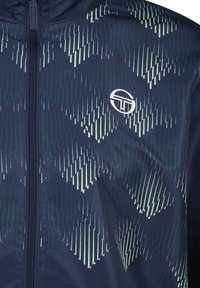 Marineblauwe zip-up jas met een vervaagd geometrisch patroon in het groen. Gemaakt van textuurstof, met een klein rond logo op de borst.
