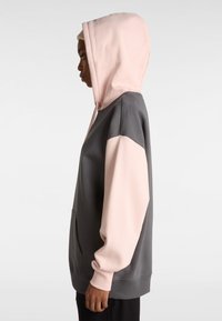 Sudadera bloqueada en gris y rosa con capucha ajustable, bolsillo canguro y puños acanalados, hecha de una tela suave. Vista lateral.