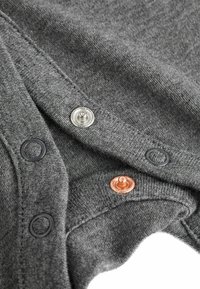 Graues Strickgewebe mit drei Knopfschlüssen: silbernes Metall, kupferähnlich und schwarzes Plastik. Sichtbare Nähdetails und glatte Textur.