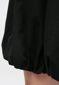 Μαύρη φούστα με φουσκωτό, ριγέ κάτω άκρο, με λεία, ματ υφή και ελαφρύ ύφασμα. Χωρίς ορατά σχέδια ή μεταλλικά στοιχεία.