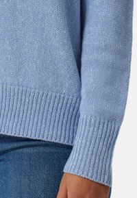 Helles blaues Strickpullover mit geripptem Saum und Bündchen, der eine strukturierte Oberfläche und ein weiches Erscheinungsbild aufweist. Das Material wirkt warm und gemütlich.