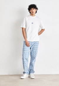 White short-sleeve t-shirt with small blue logo, paired with light blue pants featuring repeated "HUGO" branding. White sneakers complete the outfit.