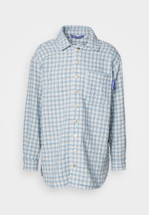 Zilgnē un baltā šķērsošanas flaneļa krekls ar garām piedurknēm, pogājamu priekšpusi, krūšu kabatu un izšūtu zīmola etiķeti uz piedurknes.