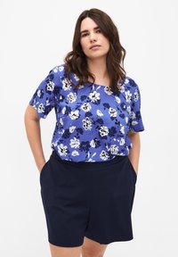 Blusa de manga corta azul con estampado de flores en blanco y azul oscuro. Combinada con pantalones cortos azul marino oscuros con bolsillos. Textura de tela suave.