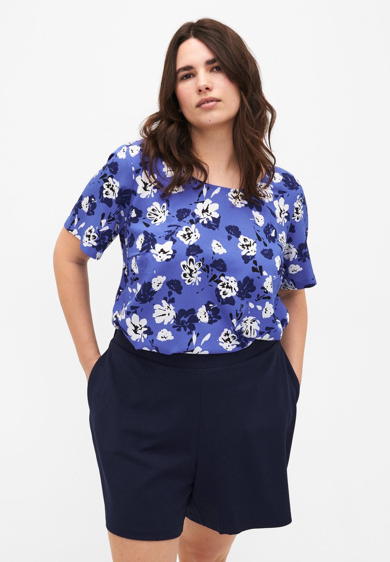 Blusa de manga corta azul con estampado de flores en blanco y azul oscuro. Combinada con pantalones cortos azul marino oscuros con bolsillos. Textura de tela suave.