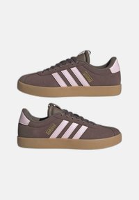 Zapatillas de ante marrón con rayas rosas, suela de goma color chicle y cordones tono sobre tono. Detalles de logo dorado en el lateral. Diseño clásico de corte bajo.