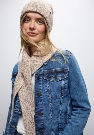 Giubbotto in denim con colletto a punta, bottoni scuri e due tasche sul petto, abbinato a una sciarpa in maglia con stampa animale beige chiaro e un berretto coordinato.