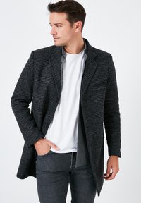 Abrigo de mezcla de lana gris con un patrón texturizado, cuello con muesca y cierre de botón frontal único, superpuesto sobre una camiseta blanca y jeans grises.