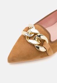 Chaussure en daim marron à bout pointu, ornée d'une chaîne dorée sur le coup de pied et d'une doublure intérieure rose pâle, présentant une texture lisse.