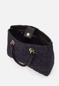 Handtas van marineblauwe gestructureerde stof met een zwart leren handvat, hardware in goudkleur en een magnetische druksluiting, met een ruime binnenkant.