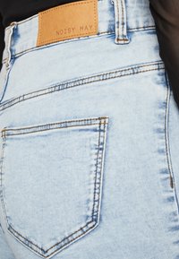 Svijetloplave traperice s džepom i smešnim šavovima, te tamna kožna oznaka brenda "NOISY MAY" na voju.