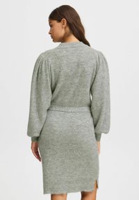 Robe tricotée en vert clair avec texture côtelée, manches bouffantes et ceinture à la taille. Présente des fentes sur les côtés au niveau de l'ourlet et un tissu doux et confortable.