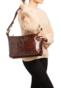 Sac à main en cuir marron avec une texture lisse, fermeture éclair et une courte bandoulière réglable. Présente des accessoires en hardware doré.