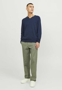 Maglione lavorato a maglia blu navy con scollo a V e polsini a costine, abbinato a pantaloni dritti verde chiaro e sneaker bianche. Design semplice.