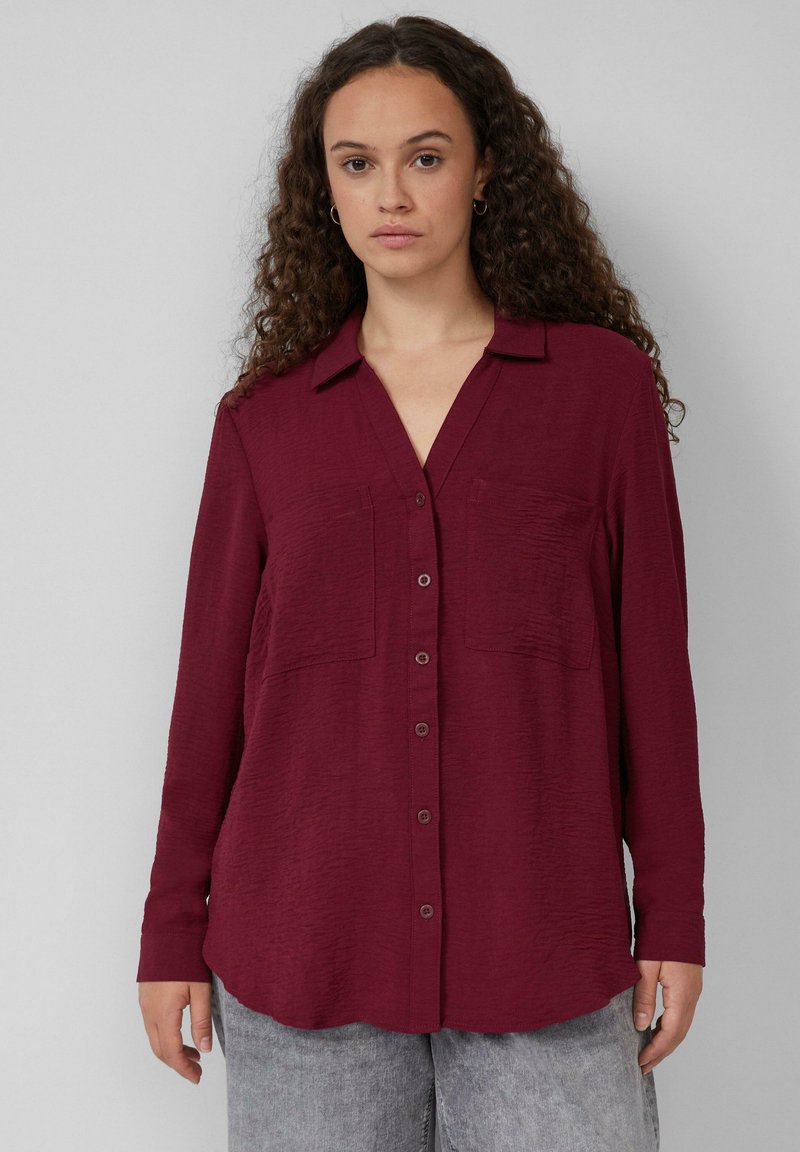 Bordeaux lange mouwen blouse met knopen van een gestructureerde stof, met een kraag en twee voorkruiszakken. Afgeronde zoom.