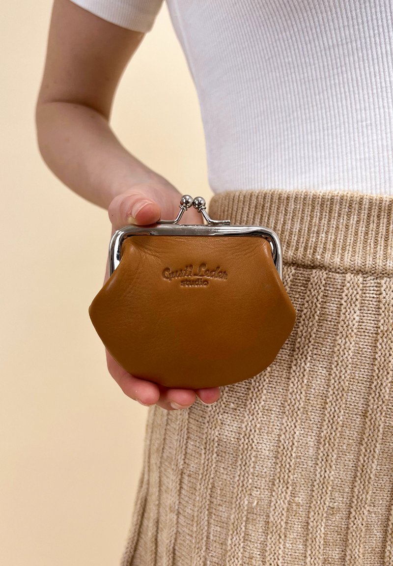 Monedero de piel marrón con forma redondeada, cierre de plata y logotipo grabado "Gastl Leder". Presenta una textura suave y un diseño minimalista.