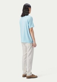Ljust blå t-shirt med kort ärm, avslappnad passform, ihop med lösa krämfärgade linnebyxor och bruna mocka slip-on skor. Neutral bakgrund.