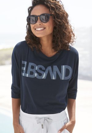 Navy long-sleeve shirt with a large light blue graphic "ELBSAND" across the front, paired with white pants featuring a drawstring waist.