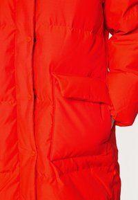 Rode pufferjack met een opvallende knoopsluiting, zijzak, gewatteerde textuur en elastische manchetten, ontworpen voor warmte en comfort.