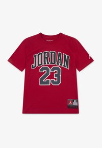 Maglietta rossa in cotone con le scritte "JORDAN" e "23" stampate in grande carattere nero. Maniche corte, scollo a girocollo, con una toppa con logo all'orlo.