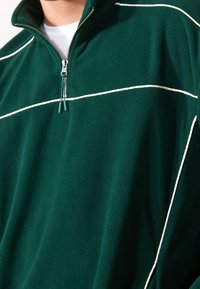 Pullover in pile verde con collo a mezza zip, caratterizzato da strisce orizzontali bianche e tessuto testurizzato per calore e comfort.