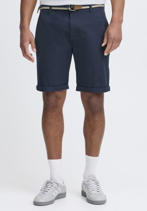 Marineblå shorts med oppbrettede ermer, laget av glatt bomullsstoff. Har et belte med en lys brun spenne og strukturerte lommer.
