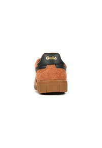 Sneaker in suede marrone con dettagli in pelle nera e suola in gomma. Presenta un tallone imbottito e un logo in rilievo sul retro.