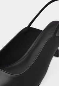 Sort lædersko med slingback, lav klods-hæl og spids tå, vist i nærbillede på hvid baggrund.