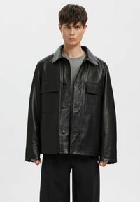 Must nahkjakk kraeulikujundusega, kinnitatav nööpidega, kahe rinnanurgaga ja lõdva lõikega. Sile tekstuur, lihtsad õmblused.