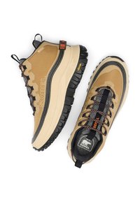 Beige vandringskängor med ett texturerat överdel, svart gummisula, färgglada skosnören och Sorel-märke. Har en styv häl och en dragflik.