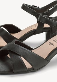 Sandalias negras de cuero con puntera abierta, tiras cruzadas, correa en el tobillo con hebilla, tacón bajo y bloque, y plantilla acolchada con la etiqueta "ancho especial".