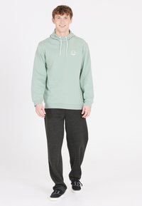 Lichtgroene hoodie met witte trekkoorden en palmboomlogo, gecombineerd met donkergrijze sweatpants en zwarte casual schoenen.