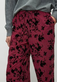 Pantaloni din material cu model floral roz și negru, cu design în carouri, având talie elastică și buzunare. Textură moale.