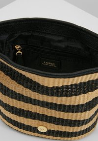 Randig vävd väska med svart och naturlig färgschema. Slät svart inredning med ficka med dragkedja och detaljer i guld.